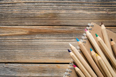 Tahta kalemler ve kahverengi kağıt geri dönüşümlü defter tahta arka planda, düz yerde. Renkli tahta kalemler, eğitici ya da okula dönüş konsepti. Boşluğu kopyala, üst görünüm.