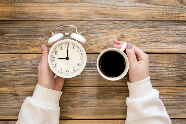 木製の背景に白い目覚まし時計と女性の手のコーヒーカップ トップビュー 創造的なコンセプト — ストック写真