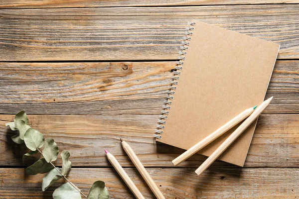 Tahta eko kalemler ve geri dönüşümlü defter. Ahşap bir arka planda, üst manzara. Çevre dostu okul kırtasiyesi.