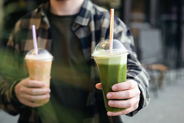 stock image A man outdoors holds a plastic glass with a green banana and mint smoothie, a delicious cooling summer drink.