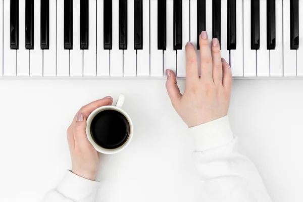 女性の手は白い背景にコーヒーカップでシンセサイザーを再生します 最小限の音楽的背景 音楽的創造性の概念 — ストック写真