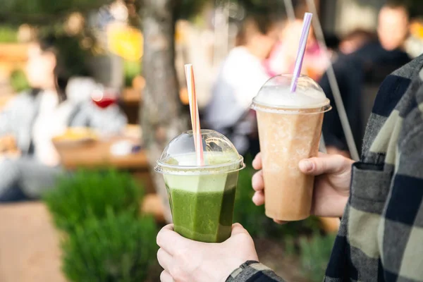 stock image Fruit smoothies in the hands of a man at a summer party, close-up. Hand holding plastic cups, health food eating lifestyle.