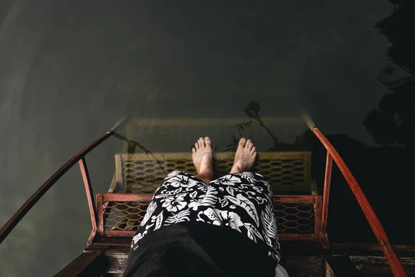 Top view of male feet at the edge of a dock with a ladder leading into dark green murky lake water.
