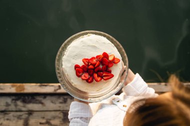 Nehrin arka planında taze çileklerle süslenmiş iştah açıcı beyaz pasta, doğada doğum günü kutlaması konsepti, üst manzara..