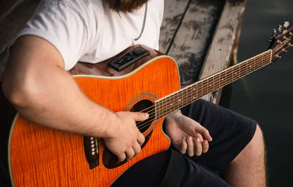 stock image A man plays the guitar sitting on a wooden pier near the lake, the concept of summer outdoor recreation.