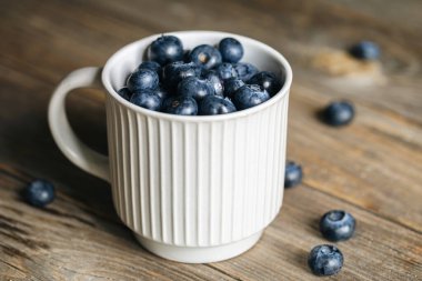 Kırsal ahşap arka planda beyaz fincanda taze çiğ organik çiftlik yaban mersini, kapat..