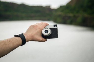 Nehrin bulanık arka planında bir erkeğin elindeki eski film kamerası, seyahat, turizm ve analog fotoğrafçılık kavramı..
