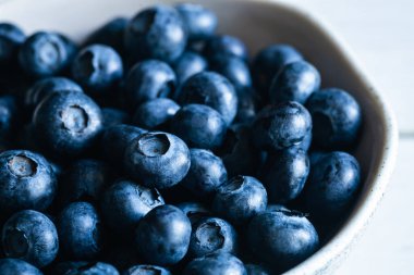 Beyaz arka planda yaban mersinli seramik beyaz kase, yakın plan, yaz meyveleri.