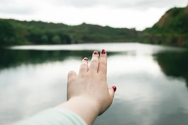 A woman stretches her hand to nature, a woman\'s hand on the background of the river, the concept of caring for nature and the environment.