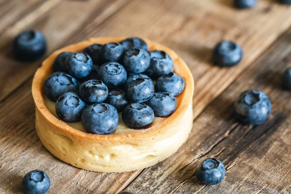 Ahşap bir arka planda yaban mersinli ve kremalı ev yapımı mini tart, yakın plan..