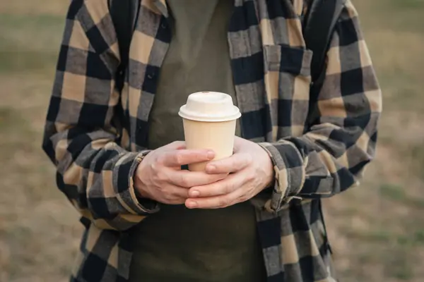 Paper cup with paper lid in male hands outside, close-up, zero waste concept, eco-friendly tableware.