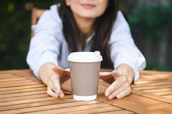 Womans hands reaching paper cup of coffee on a wooden table at the hipster coffee shop, coffee addiction concept, copy space.