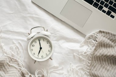 Beyaz alarm saati ve dizüstü bilgisayar, üst görünüm, yatak odasındaki beyaz çarşaflarda çalışmak..