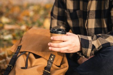 Sonbahar parkında bir adamın elinde bir fincan kağıt kahve, soğuk mevsimde sıcak bir içecek, ormanda bir yürüyüş, uzay kopyası..