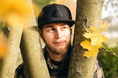 Sonbahar parkındaki çekici genç adam güneşli havanın tadını çıkarıyor, sonbahar ormanındaki portre, rahatlama, sonbahar havası..