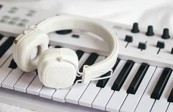 stock image White headphones on the keys of a midi keyboard in bed, a synthesizer for home practice, remote music lessons, music creation.