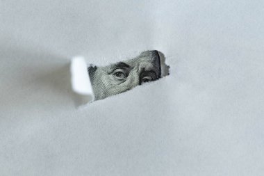 İş ve finans kavramı. Bir kağıt yaprağının yırtık deliğinde 100 dolarlık bir banknotun görüntüsü görülebilir. Benjamin Franklin 'in yüz dolarlık banknottaki yüzü..