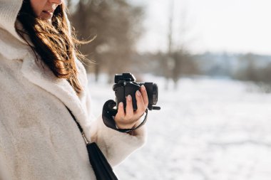 Bir kadın kışın dışarıda elinde bir kamera tutuyor. Uzayın kopyası. Bir kadının elindeki SLR kamerası karın arka planına karşı. Açık havada kış fotoğrafı çekimi..