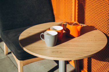 Sert gölgeli bir kafede iki fincan ve bir çaydanlık. Modern bir kafede portakallı çaydanlık ve fincanlar. Güneşli bir sabah ve bir fincan çay. Boşluğu kopyala.