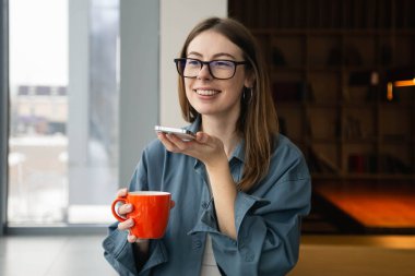 Neşeli mutlu beyaz öğrenci kütüphanede sesli mesaj kaydediyor, hoparlörden telefon görüşmesi yapıyor, konuşuyor, akıllı telefondan elektronik ses asistanına emir veriyor..