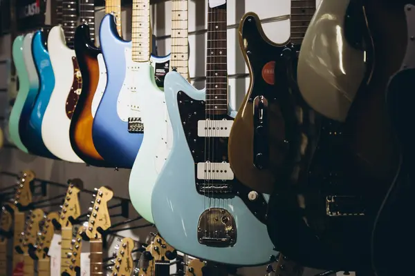 Many electric guitars hanging on wall of music shop, close up. Buying electric guitar. Stand with various colorful electric guitars in music shop.