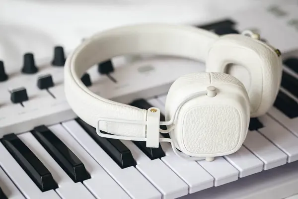 stock image White headphones on the keys of a midi keyboard in bed, a synthesizer for home practice, remote music lessons, music creation.