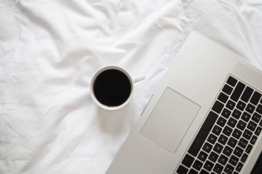 Laptop ve kahve beyaz çarşaflarda, düz yatakta, üst görünüm minimalist çalışma alanı arka planında, sabah konseptinde çalışıyor..