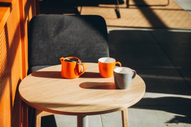 Sert gölgeli bir kafede iki fincan ve bir çaydanlık. Modern bir kafede portakallı çaydanlık ve fincanlar. Güneşli bir sabah ve bir fincan çay. Boşluğu kopyala.