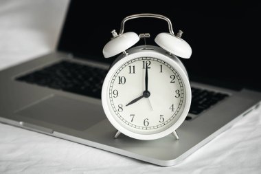 Beyaz alarmlı saat ve dizüstü bilgisayar yatak odasında beyaz çarşaflarla çalışıyor..