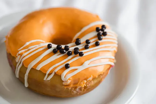 Parlak turuncu donut, jöleli ve beyaz battaniyeli çikolata toplarıyla süslenmiş..