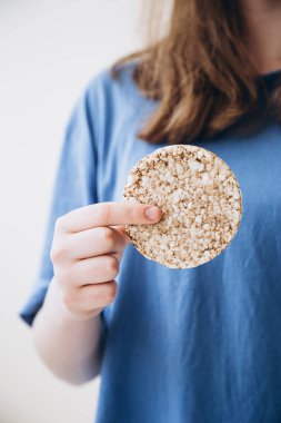 Whole grain cake, buckwheat cake, rice cake in the hands of a girl. Girl eating crunchy rice cake in her hands. Healthy food, healthy lifestyle, embracing a healthy diet. clipart