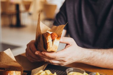Adamın elinde taze sosisli ve patates kızartması var. Fast food, abur cubur konsepti. Yemek konseptini aldatmak. Bir adam bir barda ya da kafede şişman atıştırmalıklar yiyor..