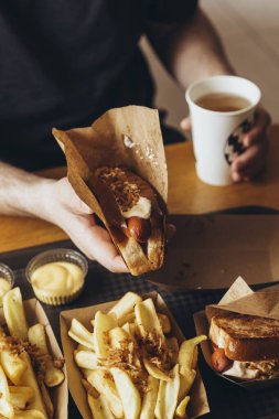 Adamın elinde taze sosisli ve patates kızartması var. Fast food, abur cubur konsepti. Yemek konseptini aldatmak. Bir adam bir barda ya da kafede şişman atıştırmalıklar yiyor..