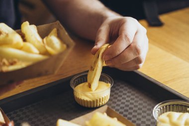 Yakından bakınca, bir adam patates kızartması yiyor. Yemek konseptini aldatmak. Yemek, yaşam tarzı konsepti. Bir erkek eli patates kızartmasını tutar ve peynir sosuna batırır. Çıtır patatesler derinde.