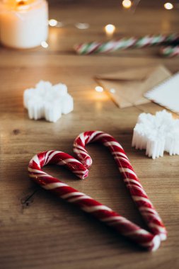 Masanın üzerinde kalp şeklinde duran iki tane kırmızı karamel Noel şekeri. Şenlikli tatlılar ve dekoratif öğeler. Samimi bir Noel geçmişi. Noel bayramı kutlaması. Yeni yıl konsepti.