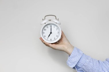 Beyaz arka planda beyaz alarmlı saati tutan kadın. - Yakın çekim. Yedi kilit. Kadın biyolojik zaman kavramı. Regl ve menopoz kavramı.