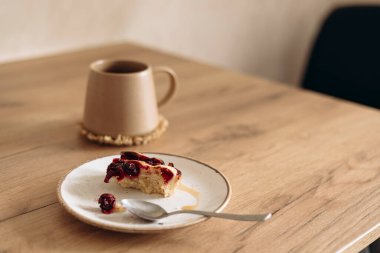 Sabahleyin mutfak masasında bir fincan kahve ve vişneli turta artığı. Sıcak ve sıcak bir atmosfer, kırsal ahşap dokular, huzurlu bir kahvaltı çağrıştırıyor ya da evde yavaş bir sabah anı..