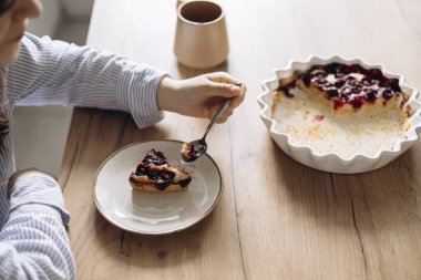 Evde bir fincan kahveyle ev yapımı vişneli turta yiyen bir kadın. Sıcak atmosfer, sıcak doğal ışık ve konfor. Yavaş yaşam temaları, ev yapımı yemekler ve günlük anlar için ideal..
