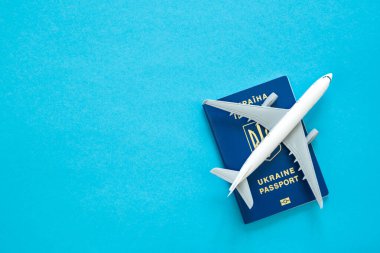 Ukrayna pasaportu ve mavi arka planda oyuncak bir plastik uçak. Ukraynalıların yurt dışına çıkışı. Boşluğu kopyala.