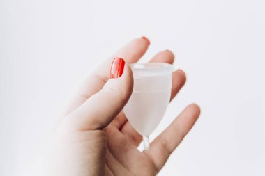 Kırmızı tırnaklı kadın eli beyaz arka planda silikon adet bardağı tutuyor. Adet görme, koruma. Kadın sağlığı konsepti. Alternatif hijyen. Sıfır atık alternatif.