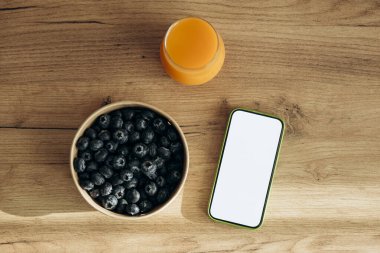 Bir bardak meyve suyu, yabanmersini ve masada boş ekran olan akıllı telefon. Kalori sayma uygulaması konsepti. Sağlıklı beslenme, şekersiz. Uzayı kopyala Temiz yemek..