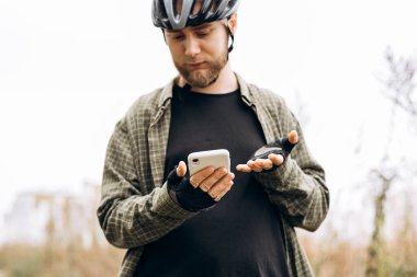 Arazide akıllı telefon kullanan bir bisikletçi. Açık hava teknolojisi, bağlantı, kırsal yaşam tarzı ve aktif özgürlük kavramı.