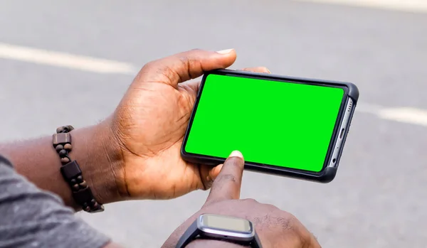 Afrikalı siyahi adam boş ekranlı akıllı telefonu işaret ediyor, akıllı saat sokak yaşam tarzı, bulanık arka plan