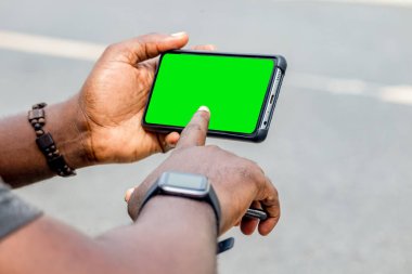 Afrikalı siyahi adam boş ekranlı akıllı telefonu işaret ediyor, akıllı saat sokak yaşam tarzı, bulanık arka plan
