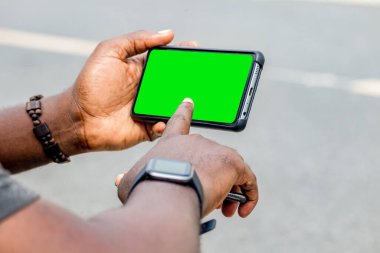 African black man pointing finger at blank screen smart phone, with smart watch street lifestyle, blurred background clipart