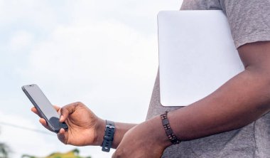 Afrikalı siyahi bir adam şehirdeki akıllı telefonu işaret ediyor, cep telefonuyla mesajlaşıyor, sokak hayatı yaşıyor, geçmişi bulanık.