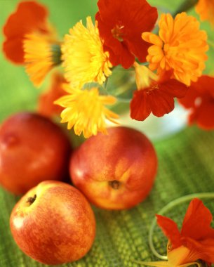 Cam bir vazoda bir kaç olgun şeftali, marygold ve nasturtium çiçeği. 