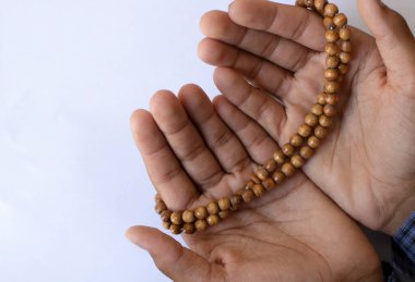 Asyalı genç çocuk beyaz bir arka planda elleri açık dua ediyor. Çocuk tespih ile Tanrı 'ya dua ediyor..