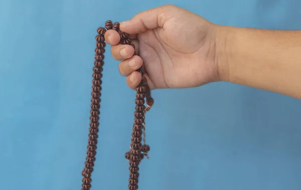 Selective focus image hand of Muslim woman holding prayer beads, the Hands of an Asian Muslim woman wearing prayer beads on blue background with copy space, Muslim woman praying with rosary beads