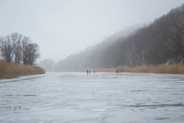 Donmuş bir kış nehrinde sis ve buzlar çözüldü. Uzakta buzdaki bir grup insan - balıkçılar